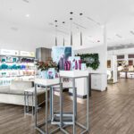 Modern salon interior with product displays, illuminated shelves stocked with hair care items, a light-colored sofa, wooden flooring, and white walls. - Salon Dulay, FL