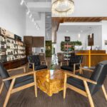 Modern salon interior featuring a wooden coffee table, four black chairs, product shelves, and a reception desk under a chandelier. - Salon Dulay, FL