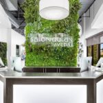 Reception desk at a modern salon with a backlit "salon dulay AVEDA" sign, surrounded by a green plant wall and sleek computer workstations. - Salon Dulay, FL