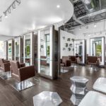 Modern hair salon with brown styling chairs, individual mirrors, and glass dividers, featuring wood flooring, exposed ceiling, and a green wall with plants. - Salon Dulay, FL