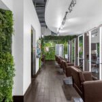 A modern hair salon with brown chairs, large mirrors, wood flooring, and green vertical plant walls for decoration. - Salon Dulay, FL