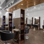 Modern hair salon interior with black styling chairs, wooden stations, mirrors, and overhead lighting. Green vertical plant wall visible on the right. - Salon Dulay, FL