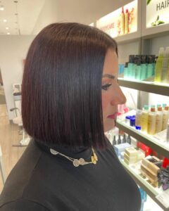 Woman with straight, shoulder-length dark hair in a blunt bob haircut, standing in a salon near shelves with hair products. - Salon Dulay, FL
