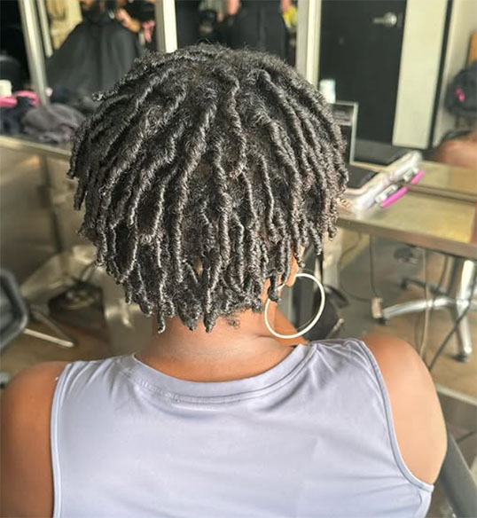 A person with short, neatly styled dreadlocks sits in a Salon Dulay chair in Orlando, surrounded by mirrors and salon tools—highlighting their expertise in Natural Hair Services. - Salon Dulay, FL